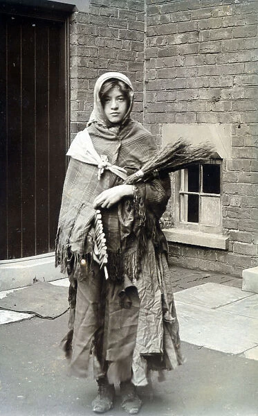 Woman dressed as winter, swaddled in rag and carrying fire wood. Date: c. 1915