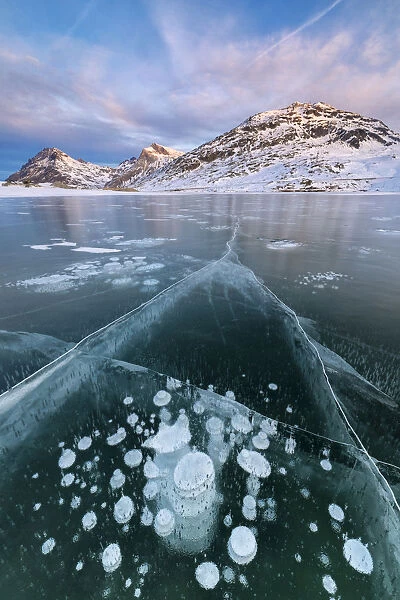Ice bubbles frame the snowy peaks reflected in Lago Bianco, Bernina Pass, canton of Graubunden