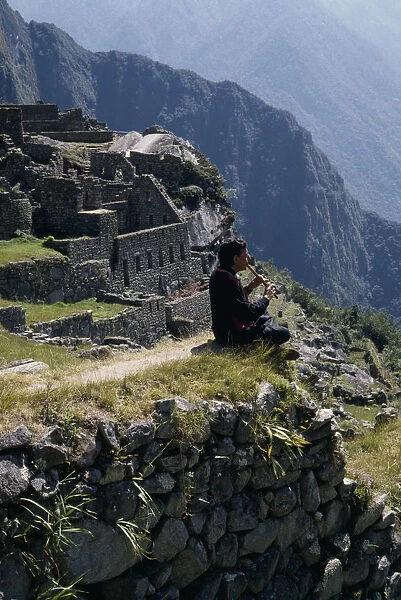 10014624. PERU Cusco Machu Picchu Piper sitting at the ruined city playing the flute Cuzco
