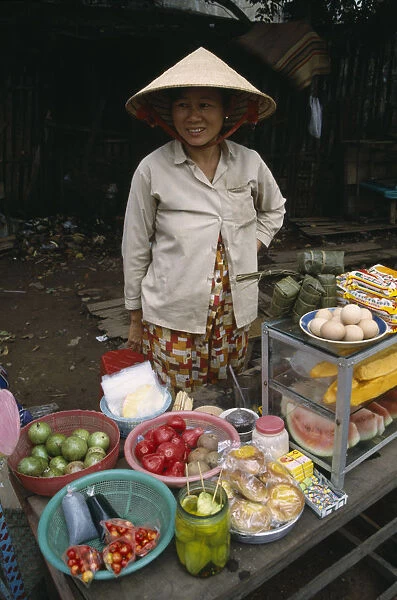 20043793. VIETNAM South Saigon Smiling woman wearing traditional conical hat selling fruit