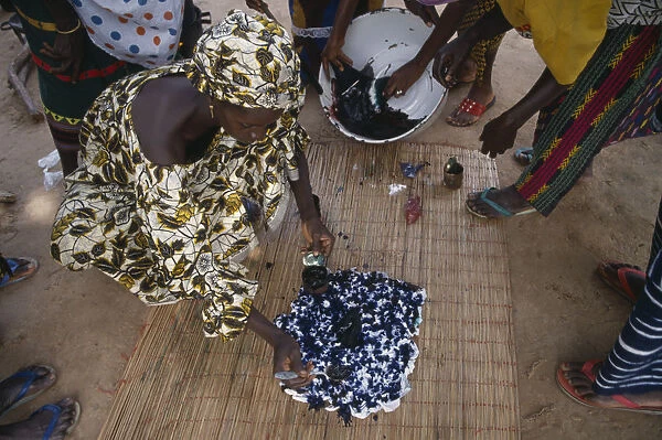 20076574. GAMBIA Arts Women applying indigo dye to cloth during tie dye process
