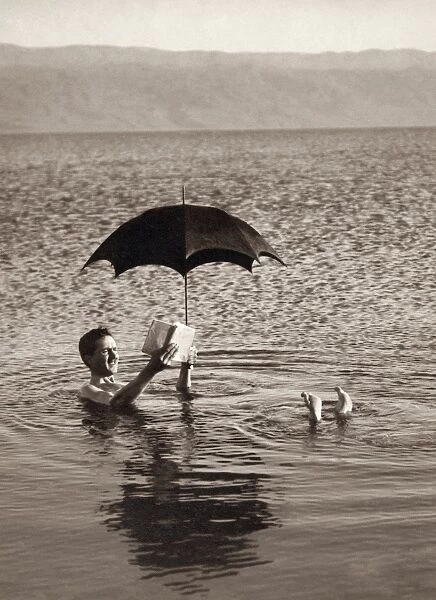 HOLY LAND: DEAD SEA. A man floating in the Dead Sea with an umbrella and a book
