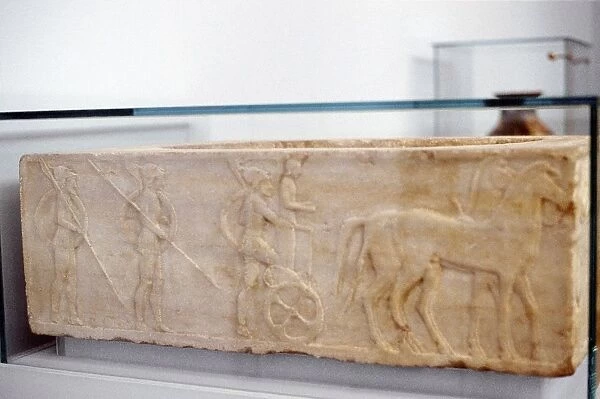 Ancient Greek warrior stepping into his chariot. Behind him are two hoplites carrying shields