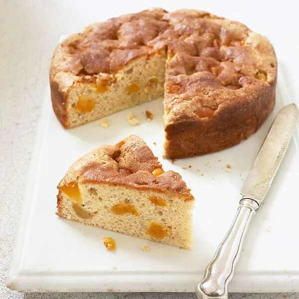 Apricot cake with single slice cut away and a silver knife nearby