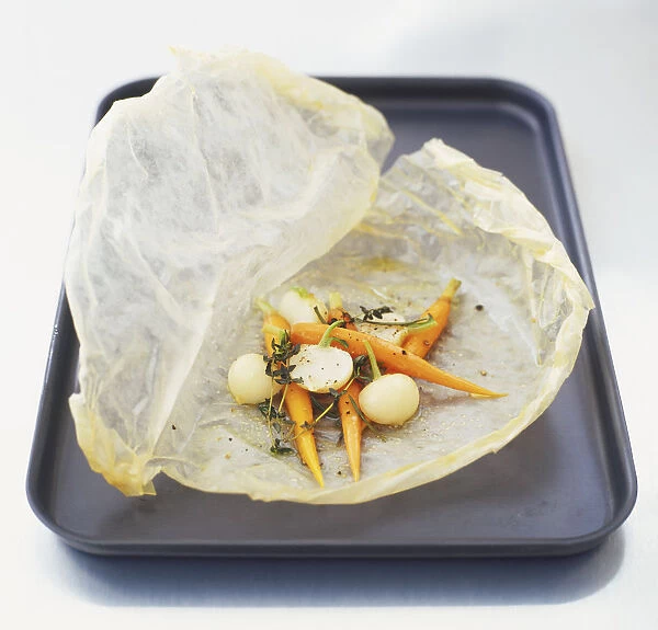 Baby carrots, turnips, sprigs of thyme and rosemary on a piece of baking parchment