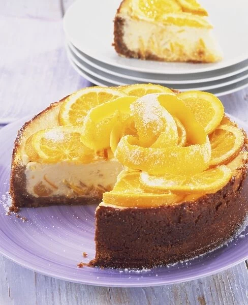 Baked St Clements cheesecake, topped with slices of orange and lemon and strips of orange and lemon zest, slice removed to show creamy inside of cake, stacked plates with slice on top in background