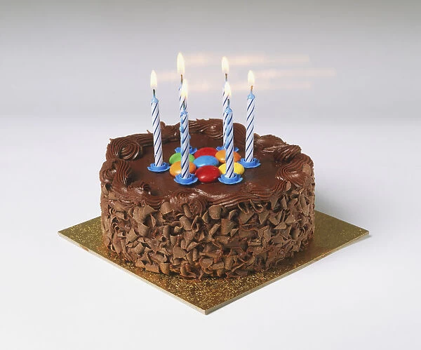 Birthday chocolate cake, decorated with chocolate shavings, multi-coloured candy and six lit candles