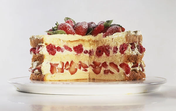 Biscuit de Savoie, layered cake with slice removed, strawberries and raspberries nestling with cream between cake layers, fresh fruit and leaves decorating top