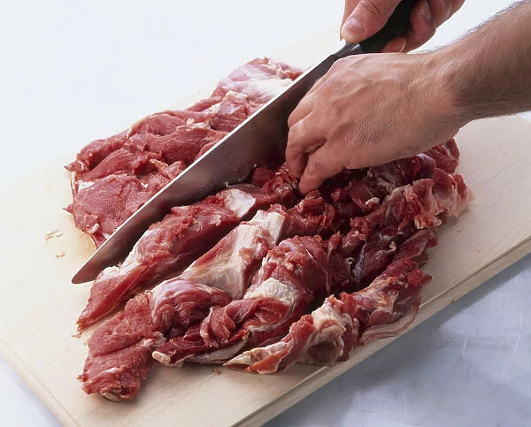 Boning leg of lamb using knife to cut through meat on either side of blade bone