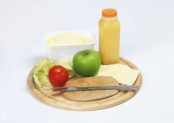 Bottle of fresh orange juice, tub of margarine, apple, tomato, lettuce leaf, wholemeal pitta bread, cheese and knife on chopping board