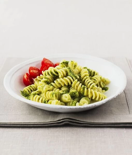 Bowl of fusilli pasta with pesto sauce and cherry tomatoes