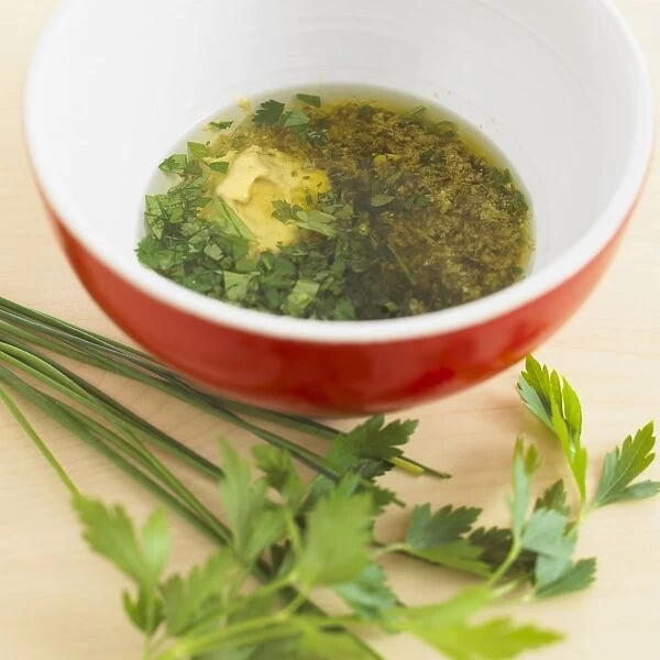 Bowl of salad dressing containing olive oil, mustard, pesto and chopped parsley, fresh parsley beside the bowl