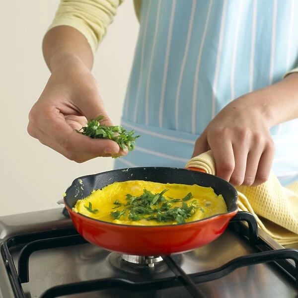 Boy adding chopped herbs to omelette in frying pan