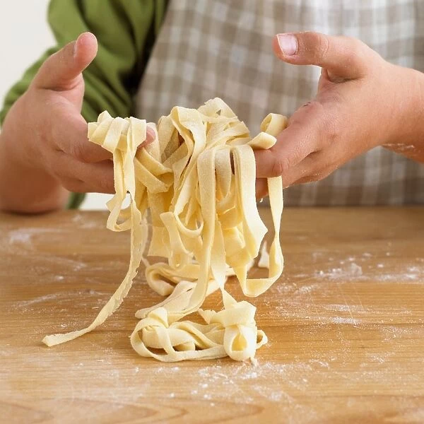 Boy picking up strands of home made tagliatelle pasta from floured surface, close-up
