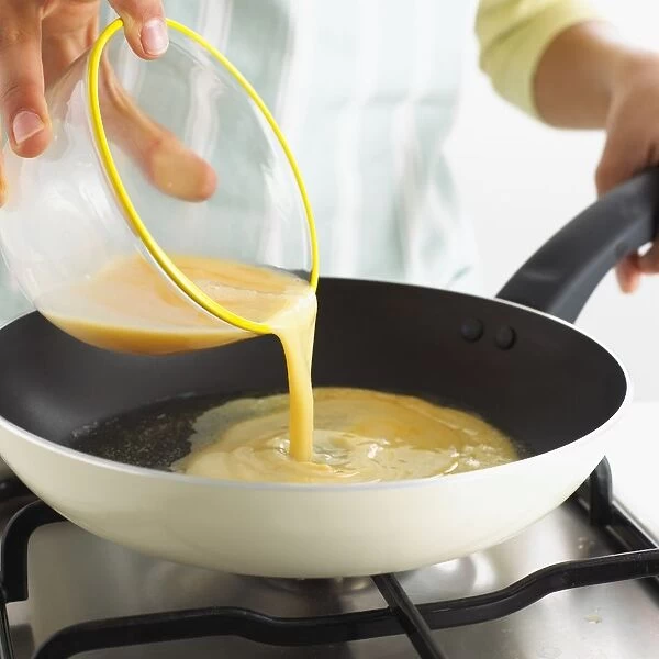 Boy pouring omelette mixture into frying pan on gas hob