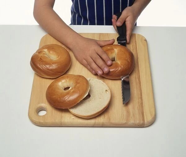 Boy using kitchen knife to cut bagel in half on wooden Choppingboard