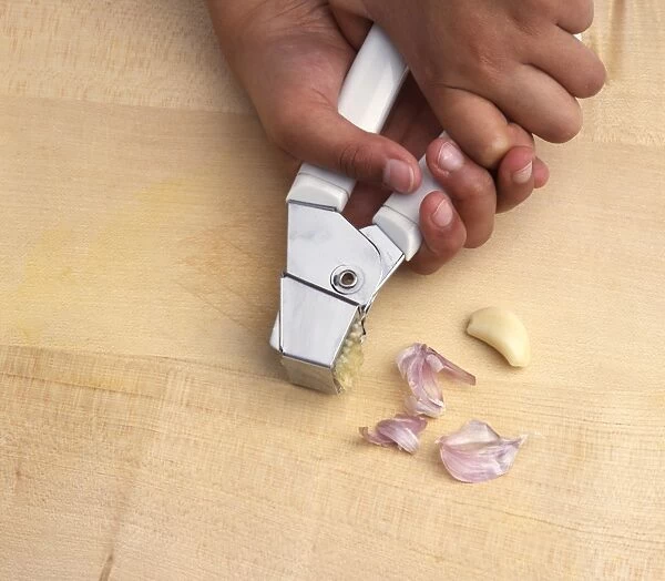 Boys hands squeezing garlic cloves through garlic press, close-up
