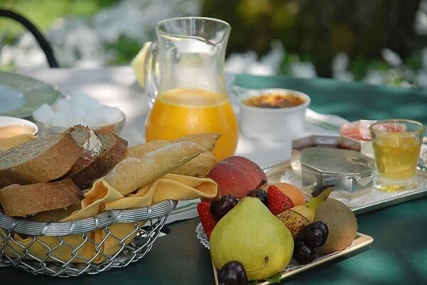 Breakfast ingredients on a table outside, including bread basket, jug of orange juice, fresh fruit