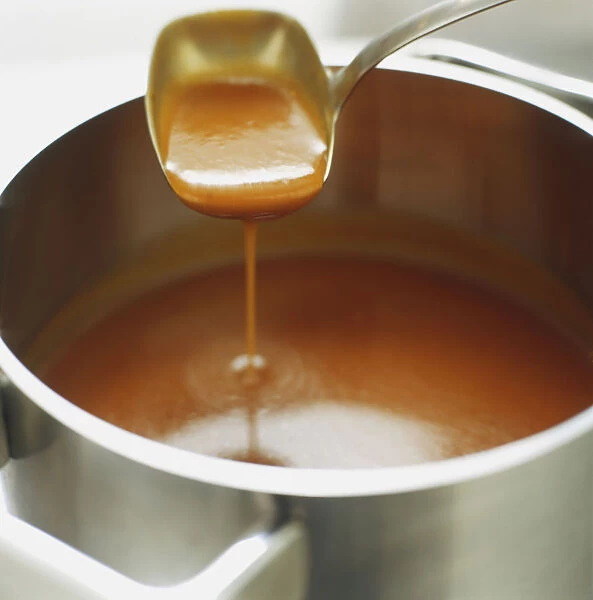 Brown sauce being ladled out of saucepan, close up