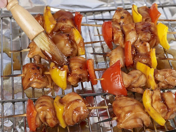 Brushing barbecue sauce onto chicken and pepper kebabs with pastry brush