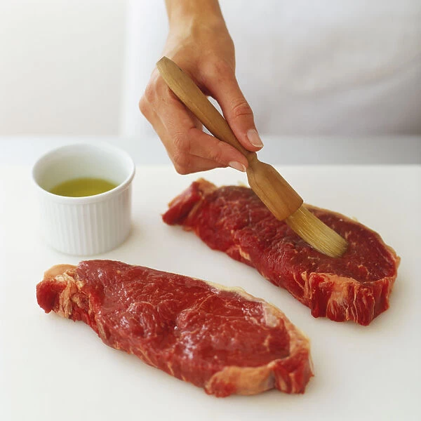 Brushing two raw steaks with oil