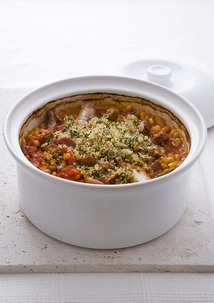 Cassoulet, a traditional dish from Southwest France, containing sausages, beans and tomatoes, topped with breadcrumbs and parsley, baked in a casserole, close-up