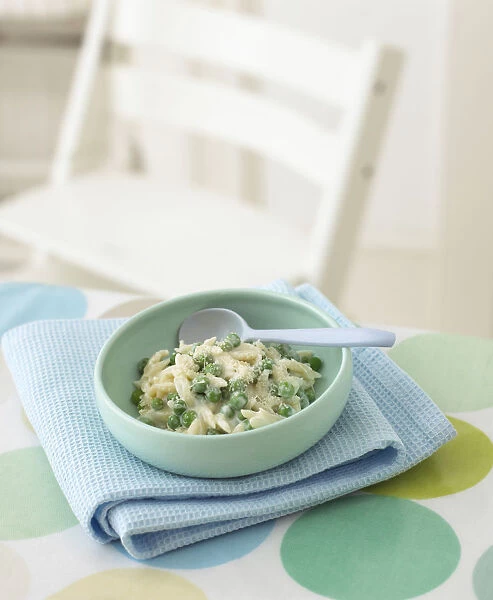 Cheese and peas orzo in bowl with spoon on top of folded blue tea towel