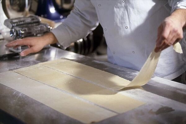 Chef placing sheet of fresh pasta on worktop, pasta machine nearby