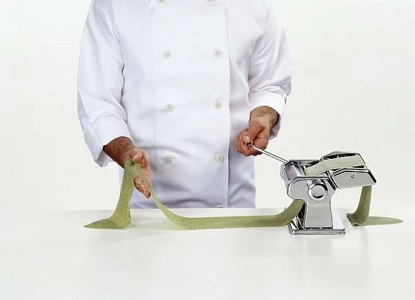 Chef rolling spinach pasta dough through a pasta machine