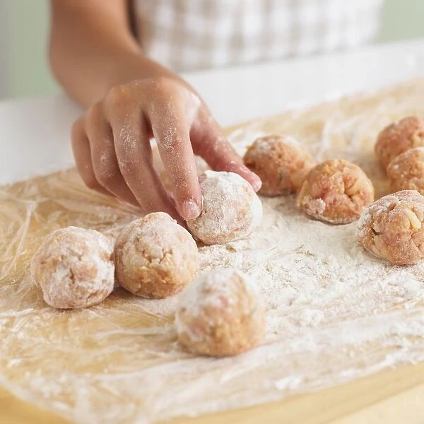 Child rolling meatballs in flour on wooden chopping board