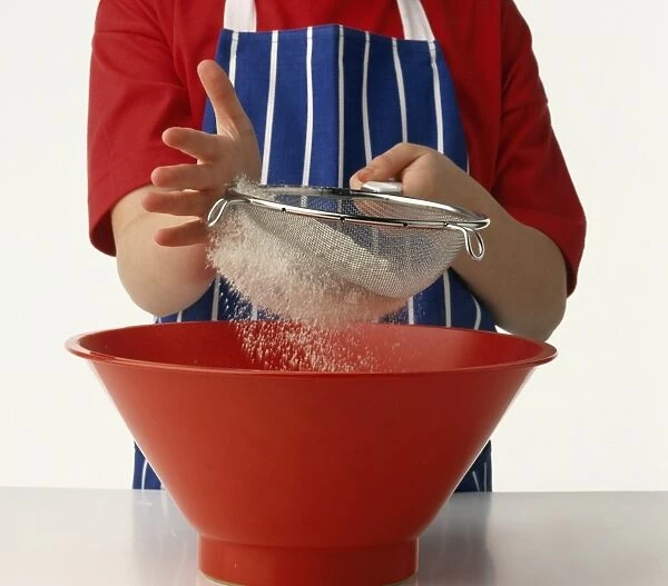 Child sifting flour into red mixing bowl