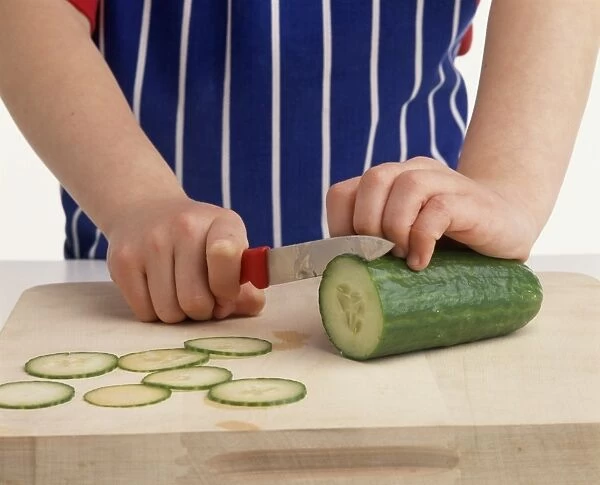 Child slicing cucumber on wooden chopping board, close-up