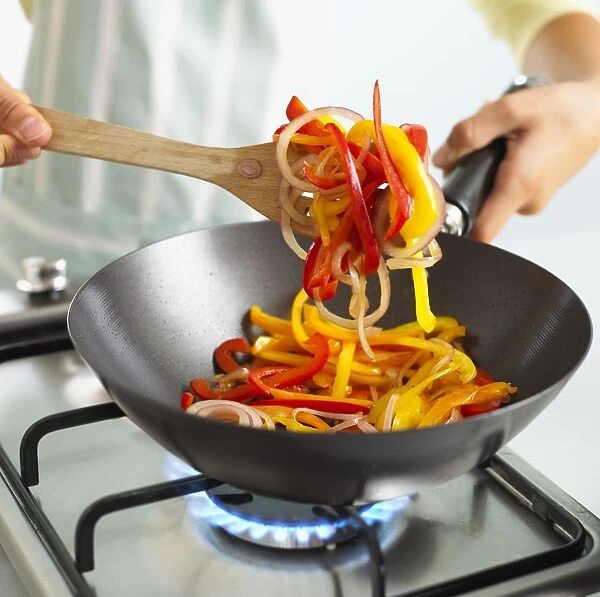 Child stirring sliced bell peppers and onions in frying pan using wooden spatula