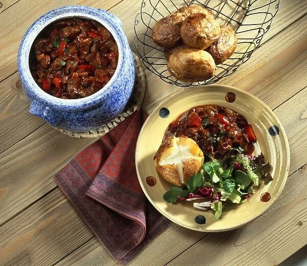 Chilli Con Carne in ceramic pot, and served on plate with jacket potatoes and salad leaves