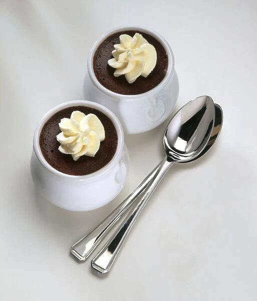 Chocolate mousse decorated with whipped cream, served in ceramic pots with two silver spoons nearby, close-up