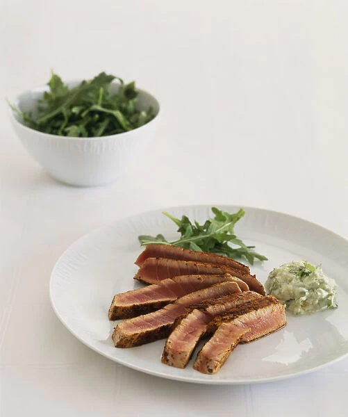 Cinnamon seared fresh tuna steak with bowl of rocket salad in background