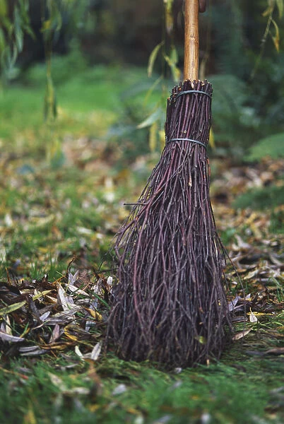 Close-up of a broomstick sweeping autumn leaves from a damp garden lawn
