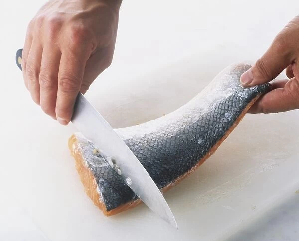 Close-up of a hand holding a knife on a salmon fillet
