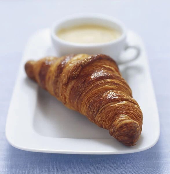 Croissant served with cup of coffee on rectangular plate, close up