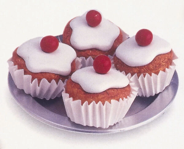 Four cupcakes covered in white fondant icing and cherries on top, served on a plate