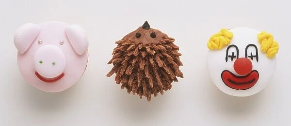 Three cupcakes decorated with the face of a pig, a clown and a hedgehog, view from above