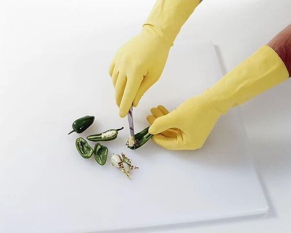 Deseeding green chilli peppers with knife, wearing rubber gloves for protection, close-up