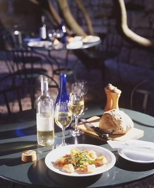 A dinner consisting of a plate of bread, a fish and vegetable dish accompanied by a bottle of white wine and two glasses