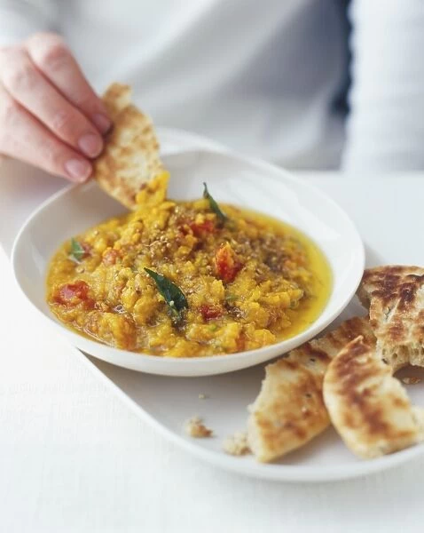 Dunking bread into an Indian stew (Dal) served in a white bowl