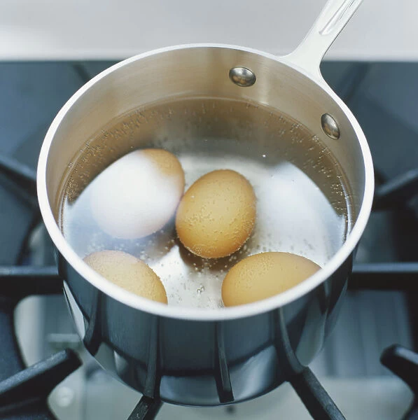 Four eggs in water inside saucepan, high angle view