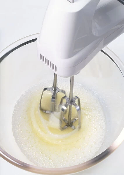 Electric mixer whisking egg whites in a glass bowl