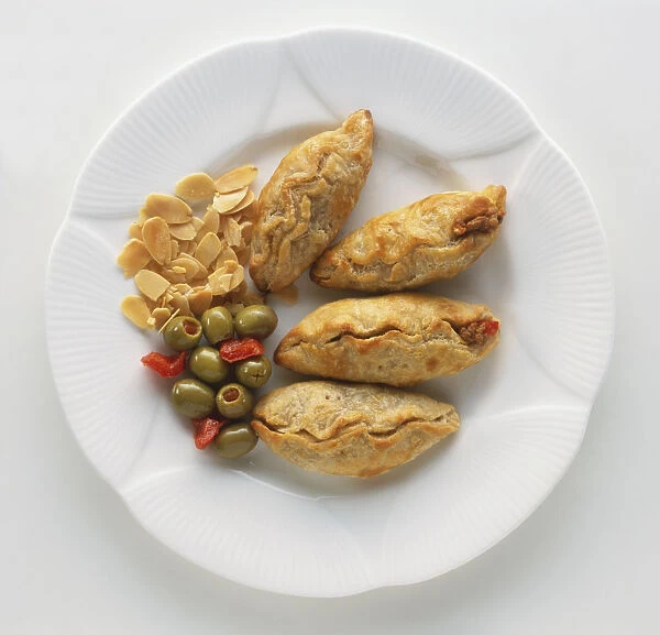 Empanaditas, four Mexican puff pastry turnovers served with stuffed olives and almond flakes on a plate