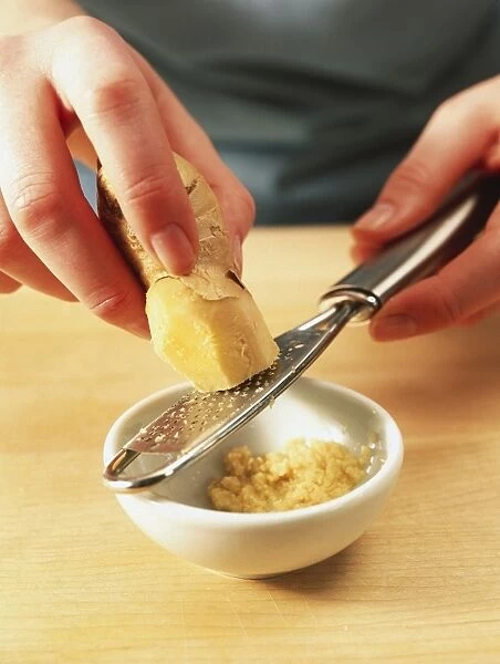 Female hand grating ginger rhizome into fine pulp with grater