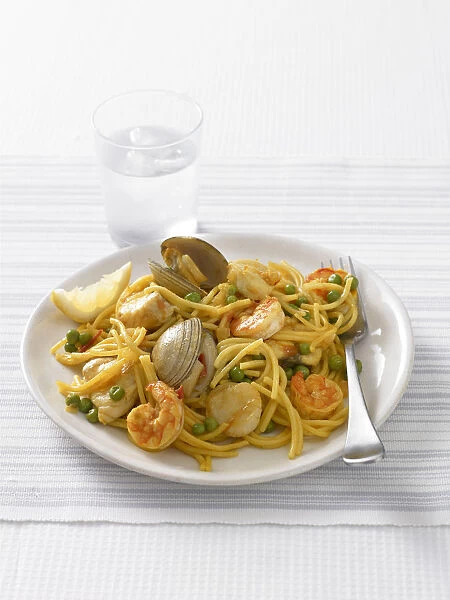 Fideua, a Spanish pasta dish of spaghetti, mixed seafood and peas, served with a glass of water, close-up