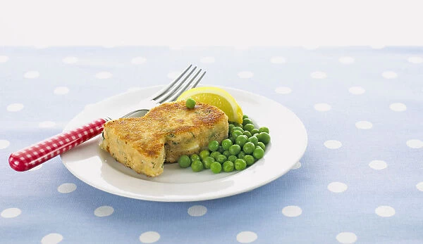 Fish-shaped fish cake with peas and lemon wedge on a plate